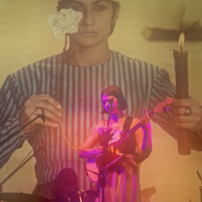 chloe corbin pink spotlight strumming guitar with image of woman projected on white wall behind